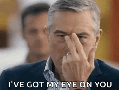 A Man In A Suit Holds His Finger To His Forehead And Says I 'Ve Got My Eye On You GIF