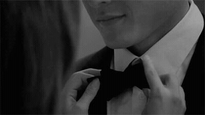 A Man In A Suit Is Adjusting His Bow Tie In A Black And White Photo GIF