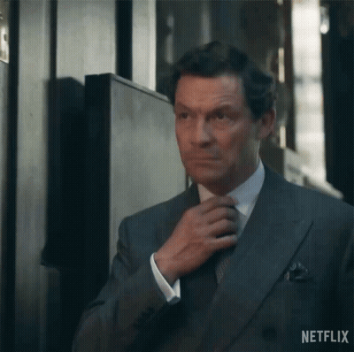 A Man In A Suit Is Adjusting His Tie In A Hallway . GIF