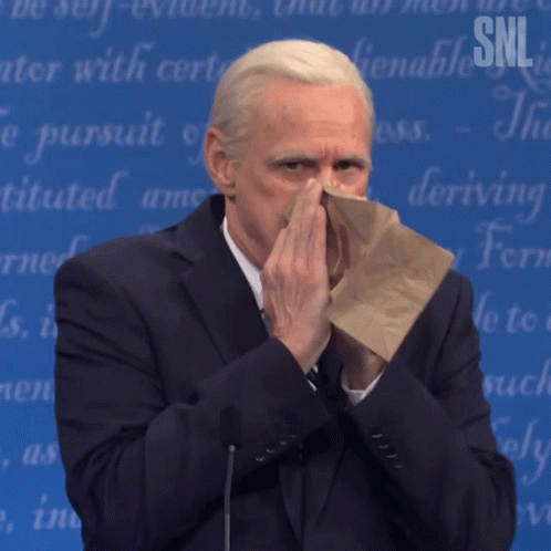 A Man In A Suit Is Blowing His Nose In Front Of A Snl Banner GIF