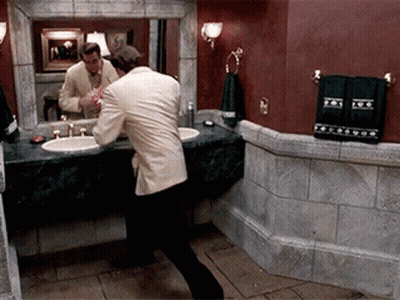 A Man In A Suit Is Brushing His Teeth In Front Of A Bathroom Mirror GIF