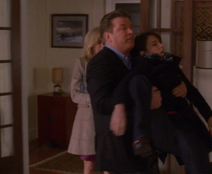 A Man In A Suit Is Carrying A Woman In A Black Coat GIF