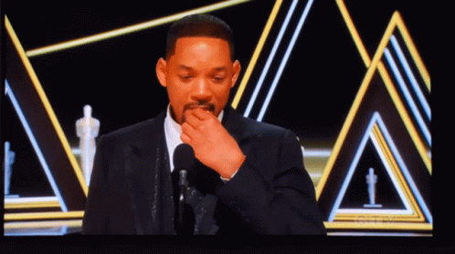 A Man In A Suit Is Covering His Mouth With His Hand GIF