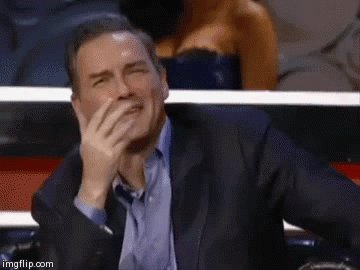 A Man In A Suit Is Covering His Mouth With His Hand While Laughing . GIF