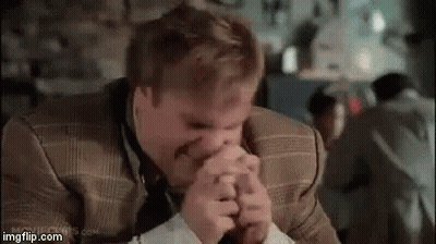 A Man In A Suit Is Covering His Mouth With His Hands . GIF
