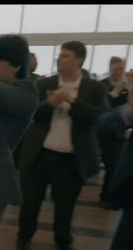A Man In A Suit Is Dancing In A Crowd Of People In A Room . GIF