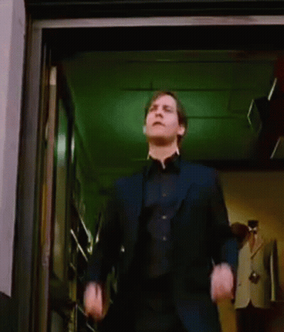 A Man In A Suit Is Dancing In A Doorway While A Woman Stands Behind Him . GIF