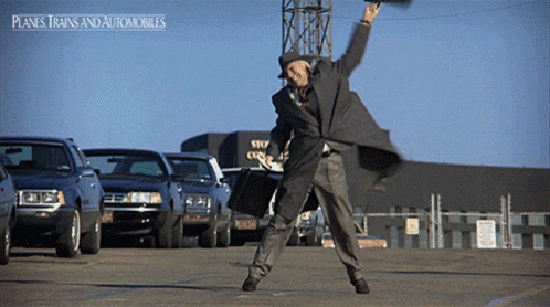 A Man In A Suit Is Dancing In A Parking Lot With Planes Trains And Automobiles Written On The Bottom GIF