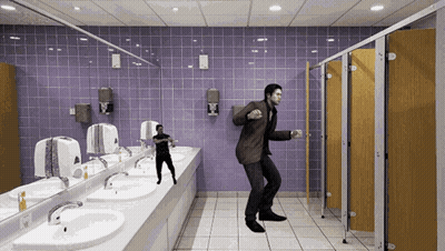 A Man In A Suit Is Dancing In A Public Bathroom GIF