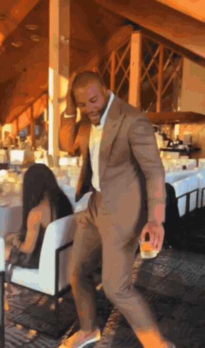 A Man In A Suit Is Dancing In A Restaurant With A Woman Sitting In A Chair Behind Him GIF