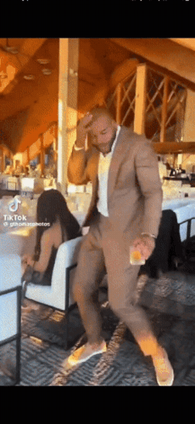 A Man In A Suit Is Dancing In A Room With A Woman Sitting In A Chair GIF