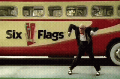 A Man In A Suit Is Dancing In Front Of A Bus That Says Six Flags . GIF