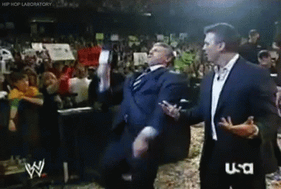 A Man In A Suit Is Dancing In Front Of A Crowd While A Man In A Suit Talks To Him .. GIF