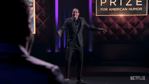 A Man In A Suit Is Dancing In Front Of A Prize For American Humor Sign GIF
