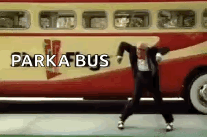 A Man In A Suit Is Dancing In Front Of A Red And Yellow Bus . GIF