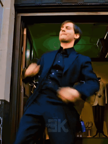 A Man In A Suit Is Dancing In Front Of A Store With The Letters Bk On The Bottom GIF