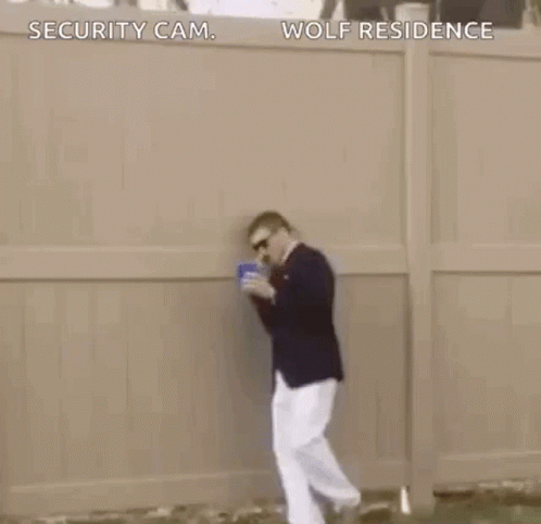 A Man In A Suit Is Dancing In The Grass While Holding A Blue Cup . GIF