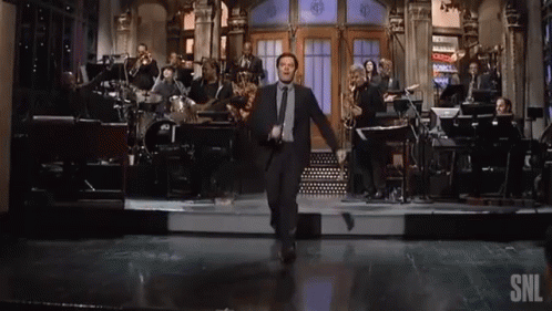 A Man In A Suit Is Dancing On A Stage With A Snl Logo In The Corner GIF