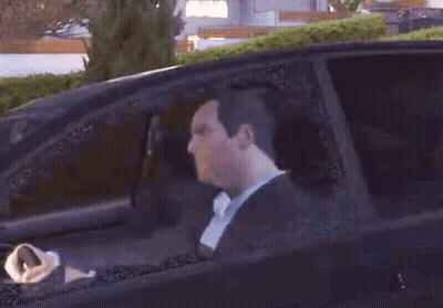 A Man In A Suit Is Driving A Car And Looking Out The Window GIF