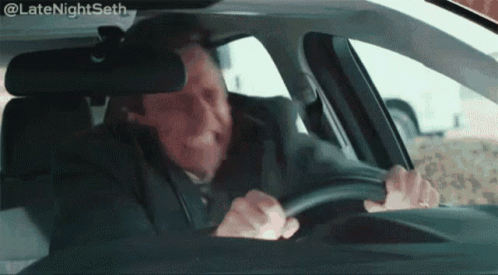 A Man In A Suit Is Driving A Car With His Mouth Open . GIF