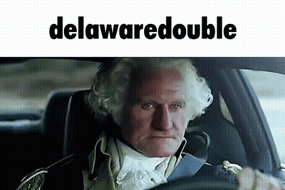 A Man In A Suit Is Driving A Car With The Word Delawaredouble On The Bottom GIF