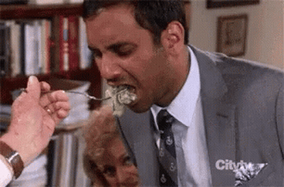 A Man In A Suit Is Eating A Piece Of Lettuce With A Fork .. GIF