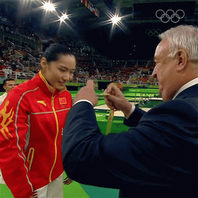 A Man In A Suit Is Giving A Medal To A Woman In A Red And Yellow Jacket GIF