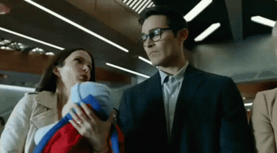 A Man In A Suit Is Holding A Baby While A Woman Holds A Baby In Her Arms . GIF