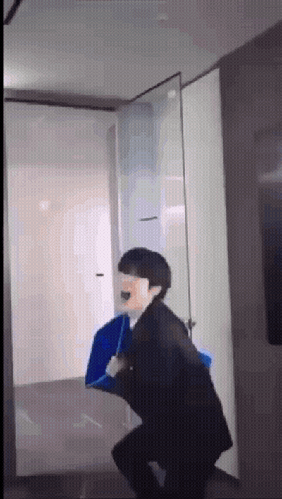A Man In A Suit Is Holding A Blue Umbrella While Standing In A Hallway . GIF