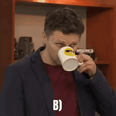 A Man In A Suit Is Holding A Coffee Mug With A Smiley Face On It And The Letter B On The Bottom GIF