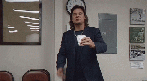 A Man In A Suit Is Holding A Cup In Front Of A Clock That Shows The Time As 10:08 GIF