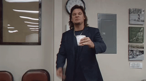 A Man In A Suit Is Holding A Cup In Front Of A Clock That Shows The Time As 8:15 GIF