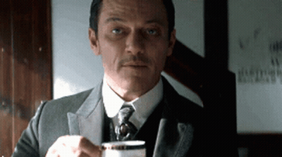 A Man In A Suit Is Holding A Cup Of Coffee GIF