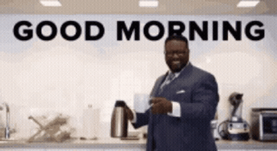 A Man In A Suit Is Holding A Cup Of Coffee In Front Of A Sign That Says Good Morning . GIF