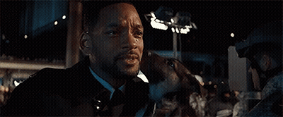 A Man In A Suit Is Holding A Dog In His Arms . GIF