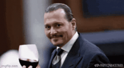 A Man In A Suit Is Holding A Glass Of Red Wine . GIF