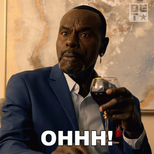 A Man In A Suit Is Holding A Glass Of Wine And Saying Ohhh GIF