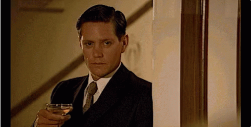 A Man In A Suit Is Holding A Glass Of Wine GIF