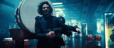 A Man In A Suit Is Holding A Gun In Front Of A Drum And A Sign That Says I.p.p. GIF