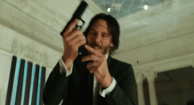 A Man In A Suit Is Holding A Gun In His Hand GIF