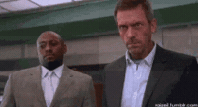 A Man In A Suit Is Holding A Large Knife While Another Man Stands Behind Him . GIF
