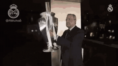 A Man In A Suit Is Holding A Large Trophy In His Hands . GIF