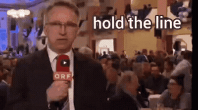 A Man In A Suit Is Holding A Microphone In Front Of A Crowd . GIF