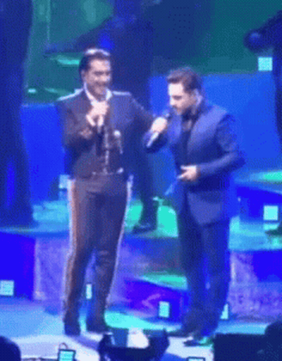 A Man In A Suit Is Holding A Microphone Next To Another Man In A Suit GIF