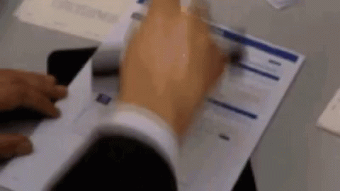 A Man In A Suit Is Holding A Piece Of Paper In His Hand . GIF