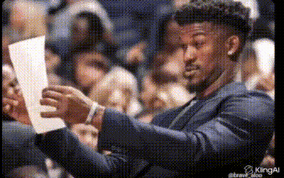 A Man In A Suit Is Holding A Piece Of Paper In His Hands . GIF