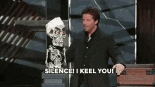 A Man In A Suit Is Holding A Puppet Of A Skeleton And Says Silence I Keel You GIF