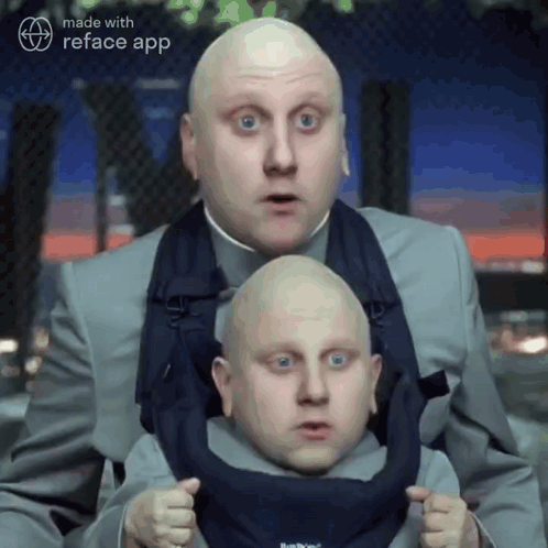 A Man In A Suit Is Holding A Smaller Man In A Baby Carrier .. GIF