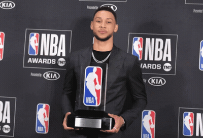 A Man In A Suit Is Holding A Trophy In Front Of A Wall That Says Nba GIF