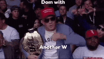 A Man In A Suit Is Holding A Ufc Championship Belt In Front Of A Crowd . GIF